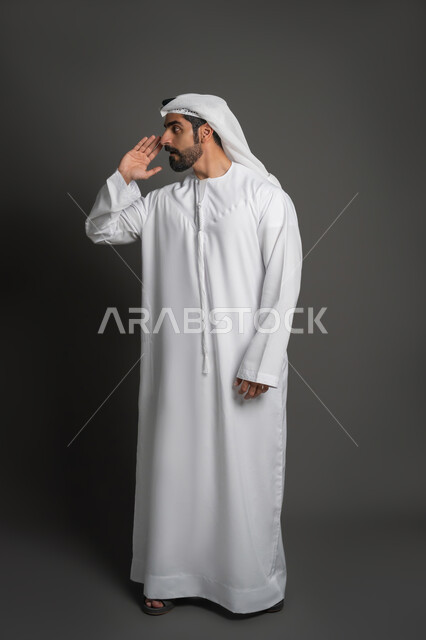 إيماءات النداء لشخص ما, بورتريه لرجل عربي إماراتي خليجي يرتدي الكندورة والغترة يرفع يده بتعابير طلب أحد ما, صورة لكامل الجسم، خلفية سوداء