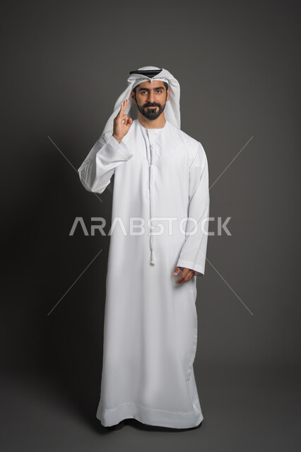 التعبير عن الجودة والاتقان، بورتريه لشاب عربي خليجي اماراتي يرتدي الكندورة والغترة البيضاء يشير بيده بإيماءات تدل على الاعجاب والقبول، علامة الجودة الامتياز والتميز، صورة لكامل الجسم، خلفية سوداء