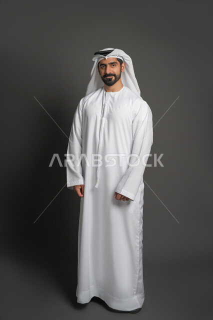 الأناقة والاهتمام بالمظهر الخارجي، الوقوف باستعداد واستقامة، مفهوم الرجولة والثقة بالنفس، التقاط الصور الشخصية للوثائق الرسمية، بورتريه لرجل عربي خليجي إماراتي يرتدي الكندورة والغترة ينظر الى الكاميرا بتعابير الحزم والجدية، صورة الجسم بالكامل، خلفية سوداء