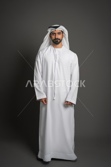 الوقوف باستعداد واستقامة، الأناقة والاهتمام بالمظهر الخارجي، مفهوم الرجولة والثقة بالنفس، التقاط الصور الشخصية للوثائق الرسمية، بورتريه لرجل عربي خليجي إماراتي يرتدي الكندورة والغترة ينظر الى الكاميرا بتعابير الحزم والجدية، صورة الجسم بالكامل، خلفية سوداء
