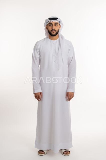 مفهوم الرجولة والاناقة، بورتريه لرجل عربي خليجي إماراتي يرتدي الكندورة والغترة يقف باستقامة وانضباط ينظر إلى الكاميرا بإيماءات الجدية والثقة بالنفس، الاهتمام بالمظهر الخارجي، صورة الجسم بالطول الكامل, خلفية بيضاء
