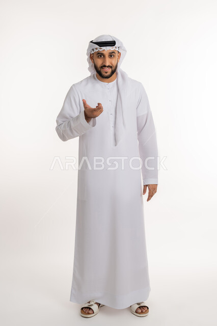 الإستفهام حول موضوع معين, بورتريه لرجل عربي خليجي إماراتي مبتسم يرتدي الكندورة والغترة ينظر الى الكاميرا يرفع يديه نحو الأعلى بإيماءات الاستفسار والتساؤل عن أمر ما، الغموض وعدم الوضوح, صورة الجسم بالطول الكامل, خلفية بيضاء