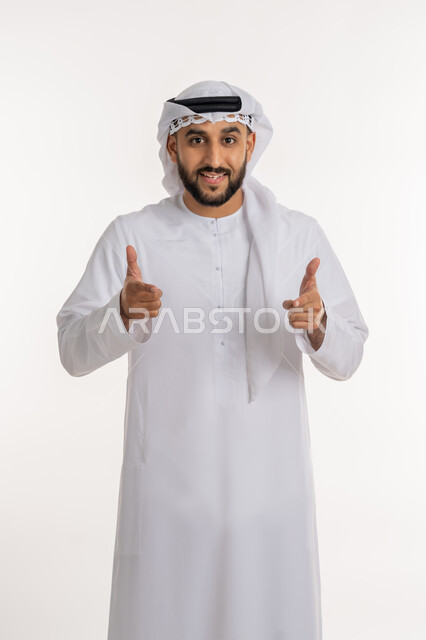 تحديد موقع معين، بورتريه لرجل عربي خليجي إماراتي مبتسم يرتدي الكندورة والغترة ينظر الى الكاميرا ييرفع يده بإيماءات الإشارة إلى شيء ما، تعابير الفرح والسرور, الاهتمام بالأناقة المظهر الخارجي، خلفية بيضاء