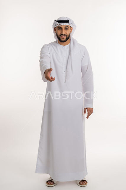إلقاء التحيه والسلام, مفهوم الاستقبال والترحيب، بورتريه لرجل عربي خليجي إماراتي مبتسم يرتدي الكندورة والغترة ينظر الى الكاميرا يمد يده بإيماءات المصافحة، التعارف و الصداقه وتكوين العلاقات, صورة الجسم بالطول الكامل، خلفية بيضاء