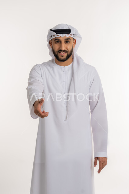 إلقاء التحيه والسلام, مفهوم الاستقبال والترحيب، بورتريه لرجل عربي خليجي إماراتي مبتسم يرتدي الكندورة والغترة ينظر الى الكاميرا يمد يده بإيماءات المصافحة، التعارف و الصداقه وتكوين العلاقات, خلفية بيضاء