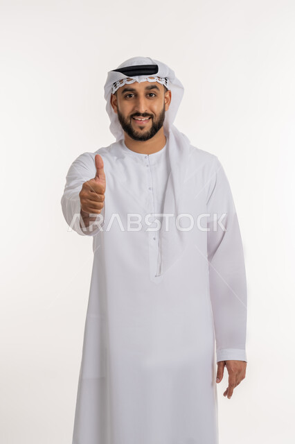 تعابير القبول والفرح والسرور، الاهتمام بالأناقة والمظهر الخارجي، بورتريه لرجل عربي خليجي إماراتي يرتدي الكندورة والغترة ينظر الى الكاميرا يرفع إصبع السبابة للاعلى بإيماءات الإعجاب والرضا، خلفية بيضاء