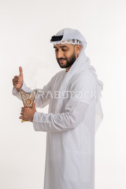 استخدام خشب العود في المناسبات والأعياد, التطيب بالروائح الفريدة، بورتريه لرجل عربي خليجي اماراتي مبتسم يرتدي الكندورة والغترة يتعطر بحامل البخور ( المبخرة ), أصالة العادات والتقاليد، الاهتمام بالأناقة والمظهر الخارجي، خلفية بيضاء