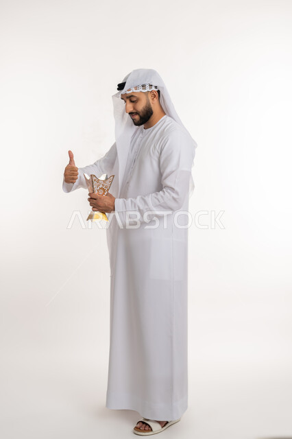 استخدام خشب العود في المناسبات والأعياد, التطيب بالروائح الفريدة، بورتريه لرجل عربي خليجي اماراتي يرتدي الكندورة والغترة يقوم بتعطير ملابسه  بحامل البخور ( المبخرة ), أصالة العادات والتقاليد، الاهتمام بالمظهر الخارجي، صورة الجسم بالطول الكامل، خلفية بيضاء