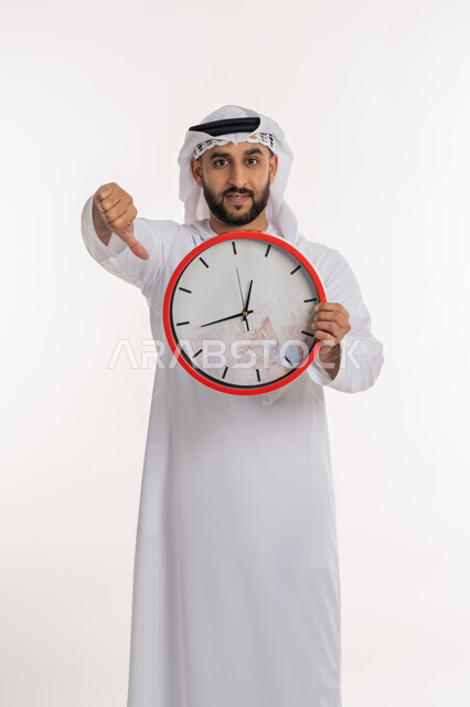 التأخير وعدم الالتزام بالمواعيد، التنبيهات والتذكيرات الثابته، بورتريه لرجل عربي خليجي اماراتي يرتدي الكندورة والغترة ينظر الى الكاميرا يحمل بيده ساعة رقمية كبيرة يرفع إصبع السبابة الى الاسفل بإيماءات عدم الرضا, خلفية بيضاء