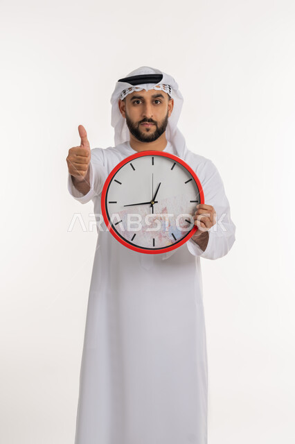 التذكيرات والتنبيهات الثابته، الدقة في المواعيد، بورتريه لرجل عربي خليجي اماراتي يرتدي الكندورة والغترة ينظر الى الكاميرا يحمل بيده ساعة رقمية كبيرة يرفع اصبع الابهام بعلامة الاعجاب والرضا, إنجاز المهامات في الوقت، خلفية بيضاء
