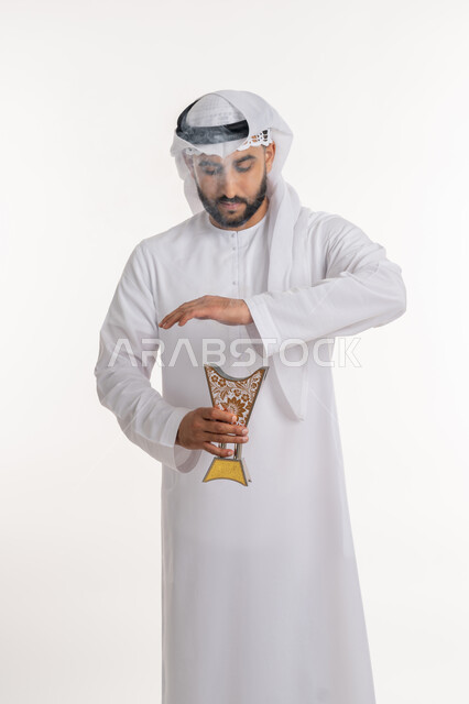 استخدام خشب العود في المناسبات والأعياد, التطيب بالروائح الفريدة، بورتريه لرجل عربي خليجي اماراتي يرتدي الكندورة والغترة يتعطر بحامل البخور ( المبخرة ), أصالة العادات والتقاليد، خلفية بيضاء