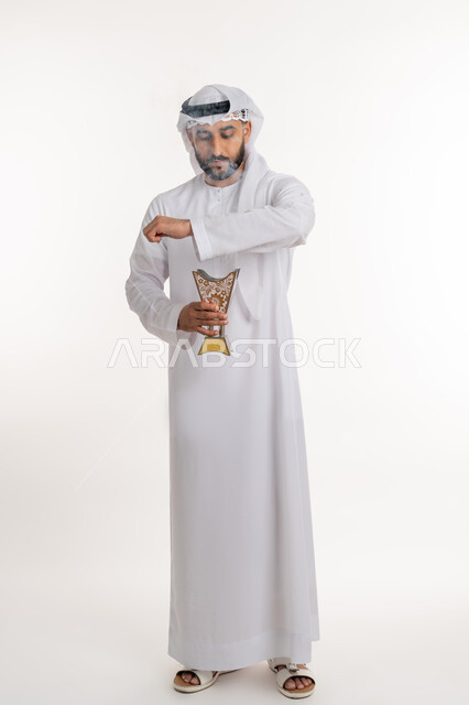 استخدام خشب العود في المناسبات والأعياد, التطيب بالروائح الفريدة، بورتريه لرجل عربي خليجي اماراتي يرتدي الكندورة والغترة يتعطر بحامل البخور ( المبخرة ), أصالة العادات والتقاليد، صورة الجسم بالطول الكامل، خلفية بيضاء