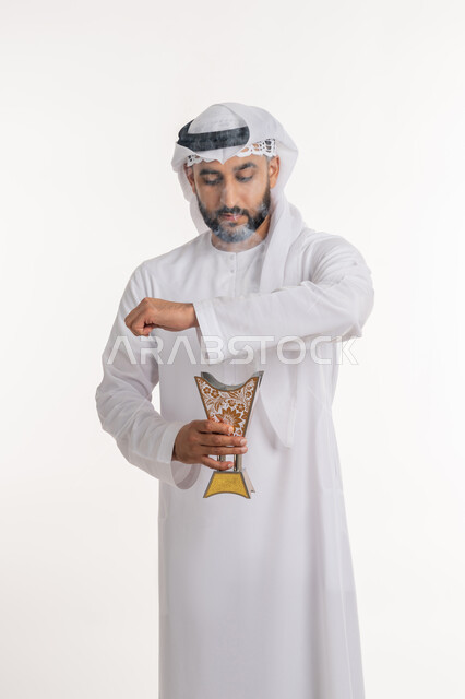 استخدام خشب العود في المناسبات والأعياد, التطيب بالروائح الفريدة، بورتريه لرجل عربي خليجي اماراتي يرتدي الكندورة والغترة يتعطر بحامل البخور ( المبخرة ), أصالة العادات والتقاليد، خلفية بيضاء