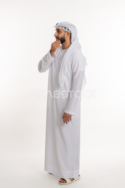 Focusing and contemplating to find a solution to a problem, portrait of an Arab Gulf Emirati man wearing a kandora and ghutra, placing his hand on his chin with gestures of thinking about something, contemplating and planning for the future, full-length body portrait, white background