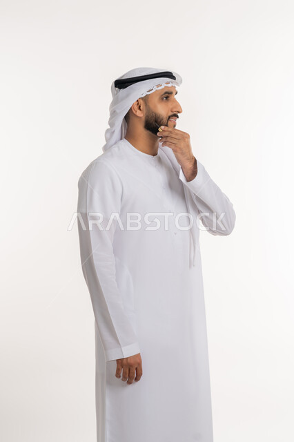 Contemplation and concentration to find a solution to a problem, portrait of an Arab Gulf Emirati man wearing a kandora and ghutra, placing his hand on his chin with gestures of thinking about something, contemplating and planning for the future, white background