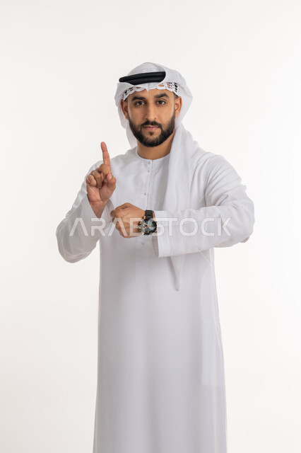 تحديد مواعيد العمل، إدارة الجداول الزمنية، بورتريه لرجل عربي خليجي اماراتي يرتدي الكندورة والغترة يرتدي ساعة اليد ينظر الى الكاميرا يرفع اصبع السبابة للاعلى بالدلالة على رقم واحد، تنظيم ومراقبة الوقت، خلفية بيضاء