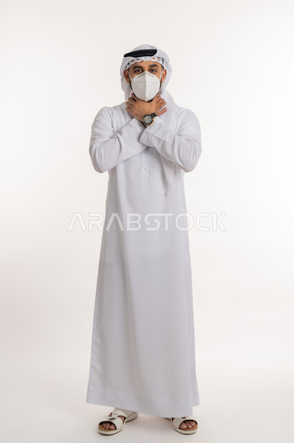 صعوبة التنفس والتعب والألم، العدوى بفايروس كورونا، بورتريه لرجل عربي خليجي اماراتي يرتدي الكندورة والغترة والكمامة الواقية ينظر الى الكاميرا يضع يديه على حلقه يشعر بالاختناق، الاصابة بنزلة برد والتهاب الحلق، صورة الجسم بالطول الكامل, خلفية بيضاء