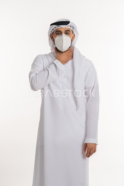 صعوبة التنفس والتعب والألم، العدوى بفايروس كورونا، بورتريه لرجل عربي خليجي اماراتي يرتدي الكندورة والغترة والكمامة الواقية ينظر الى الكاميرا يضع يديه على حلقه يشعر بالاختناق، الاصابة بنزلة برد والتهاب الحلق، خلفية بيضاء