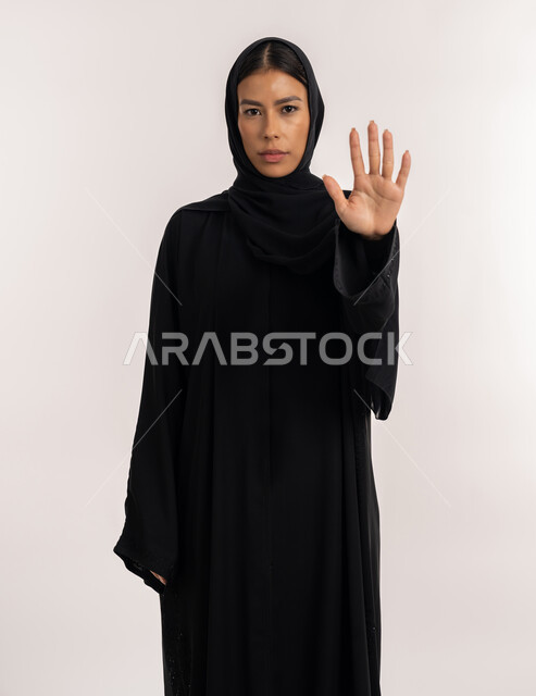 الوقوف باستقامة و اعتدال, حركات الرفض و الامتناع, بورتريه لامرأة عربية خليجية إماراتية ترتدي العباءة السوداء تنظر إلى الكاميرا بتعابير الجدية و الحزم, شابة سعودية تشير بيدها بإيماءات طلب التوقف و عدم الاقتراب, خلفية بيضاء
