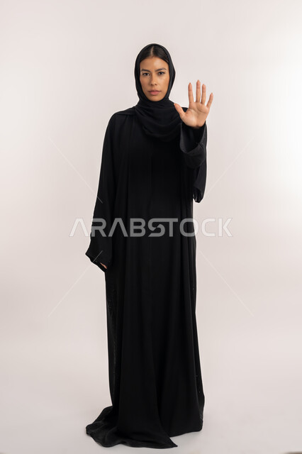 حركات الرفض و الامتناع, الوقوف باستقامة و اعتدال, بورتريه لامرأة عربية خليجية إماراتية ترتدي العباءة السوداء تنظر إلى الكاميرا بتعابير الجدية و الحزم, شابة سعودية تشير بيدها طلب التوقف و عدم الاقتراب, صورة للجسم بالطول الكامل, خلفية بيضاء