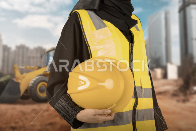 A Saudi Arabian Gulf architect, a veiled architect, wears a safety suit at work, holding a work helmet in her hand, the background of a building and construction land