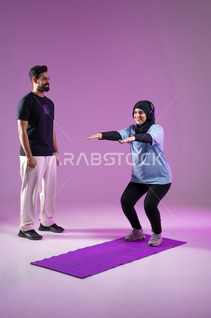 مد اليدين للامام استعداداً للقيام بحركة السكوات،بورتريه لشابة عربية خليجية سعودية ترتدي سماعه الهيدفون أثناء ممارسة الرياضة ،اسلوب حياة صحي، مفهوم الرشاقة واللياقة البدنية، انشطة ورياضات لتقوية العضلات,  المحافظة على التوازن الجسدي, خلفية بنفسجية