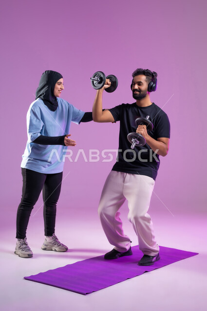 مدربة تشرح الطريقة الصحيحة لرفع الاثقال، بورتريه لشاب عربي خليجي سعودي يرتدي سماعه الهيدفون أثناء ممارسة الرياضة ،اسلوب حياة صحي، مفهوم الرشاقة واللياقة البدنية، انشطة ورياضات لتقوية العضلات,  المحافظة على التوازن الجسدي, خلفية بنفسجية