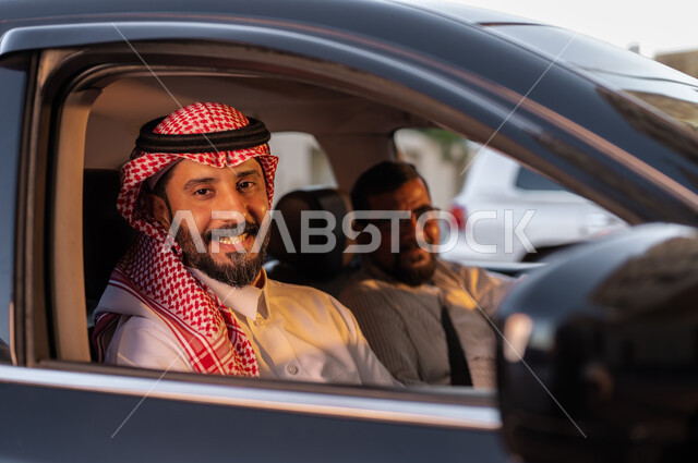 Saudi professions and jobs, recruiting workers from abroad, a close-up photo of a Saudi Arab man wearing a shemagh and traditional dress with a Pakistani driver sitting in the car looking at the camera with happy gestures, the concept of driving and delivering