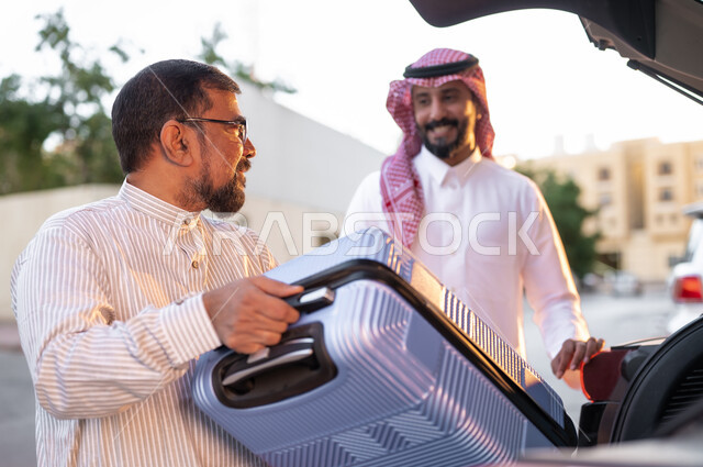 قضاء رحلات ممتعه في أوقات الفراغ ,مفهوم السياحة والسفر, صورة مقربة لرجل يرتدي الزي الباكستاني و النظارات الطبيه يقوم أمتعه رجل سعودي في السيارة, استقطاب العمالة من الخارج, خدمات النقل المريحة و الآمنة، وسائل النقل و المواصلات
