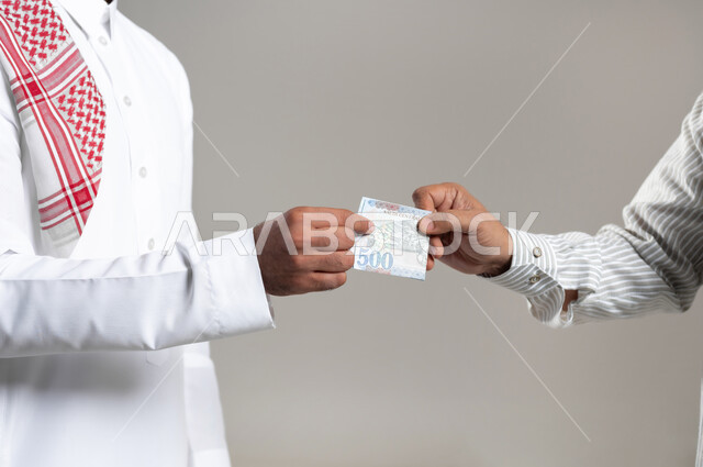 مفهوم تقدير جهد العمال, بورتريه مقرب لرجل عربي خليجي سعودي يرتدي الزي التقليدي يقوم بدفع الاجور لسيد باكستاني, استقطاب العمالة من الخارج, تقديم المستحقات المالية ,خلفية رمادية