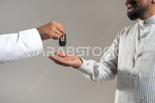 استقطاب العمالة من الخارج، مهن ووظائف سعودية، بورتريه مقرب لأيدي رجل خليجي سعودي يقوم بتسليم مفاتيح السيارة الى سائق باكستاني، مفهوم اتقان العمل, خلفية رمادية