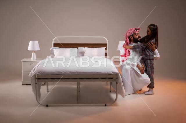 تقوية رابط الأبوة بين الأب وطفلته، ممارسة الأنشطة الترفيهية المسلية، تحمل المسؤولية والعناية بالابناء، قضاء أوقات ممتعة مع الاولاد، بورتريه لرجل عربي خليجي سعودي يقوم باحتضان ابنته وملاطفتها، صورة لكامل الجسم، خلفية ملونة