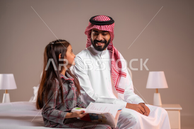 قضاء وقت ممتع مع الابنه، مفهوم التربيه القائمه على الحب والحنان، المشاركه بقراءه القصص المفيده مع الأبناء قبل النوم، بورتريه لرجل عربي خليجي سعودي يرتدي الثوب التقليدي والشماغ يجلس على السرير برفقه ابنته يقرأ الروايات المسليه، خلفية ملونة