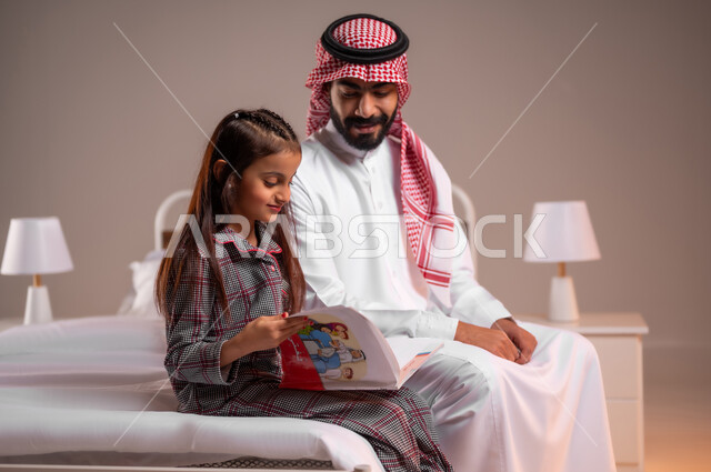 مفهوم التربيه القائمه على الحب والحنان، قضاء وقت ممتع مع الابنه، المشاركه بقراءه القصص المفيده مع الأبناء قبل النوم، بورتريه لرجل عربي خليجي سعودي يرتدي الثوب التقليدي والشماغ يجلس على السرير برفقه ابنته يقرأ الروايات المسليه، خلفية ملونة