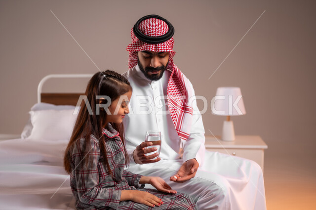الاهتمام بصحة الابناء، المحافظة على سلامة الجهاز المناعي للجسم، المداومة على شرب المياه، الشعور بالعطش والجفاف، بورتريه مقرب لأب عربي خليجي سعودي يجلس على السرير يقوم بتقديم كوب ماء زجاجي لابنته، خلفية ملونة