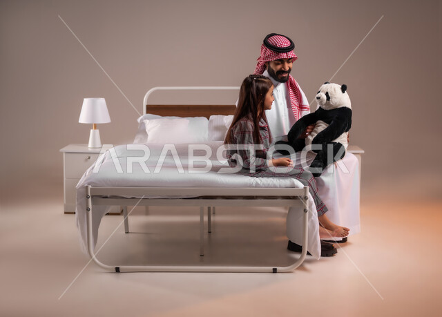 ممارسة الأنشطة الترفيهية المسلية، تحمل المسؤولية والعناية بالابناء، تقوية رابط الأبوة بين الأب وطفلته، قضاء أوقات ممتعة مع الاولاد، بورتريه لرجل عربي خليجي سعودي يقوم باللعب بدمية الدب مع ابنته، خلفية ملونة