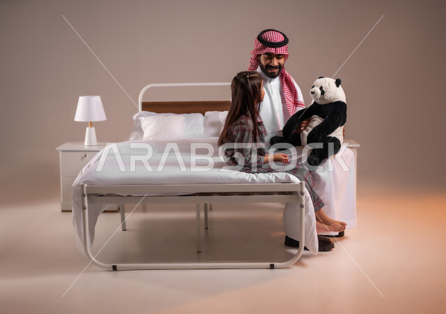 تحمل المسؤولية والعناية بالابناء، تقوية رابط الأبوة بين الأب وطفلته، قضاء أوقات ممتعة مع الاولاد، ممارسة الأنشطة الترفيهية المسلية، بورتريه لرجل عربي خليجي سعودي يقوم باللعب بدمية الدب مع ابنته، خلفية ملونة