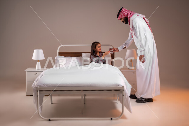 الاهتمام بصحة الابناء، المداومة على شرب المياه، المحافظة على سلامة الجهاز المناعي للجسم، الشعور بالعطش والجفاف، بورتريه لاب عربي خليجي سعودي يجلس على السرير يقوم بتقديم كوب ماء زجاجي لابنته، خلفية ملونة