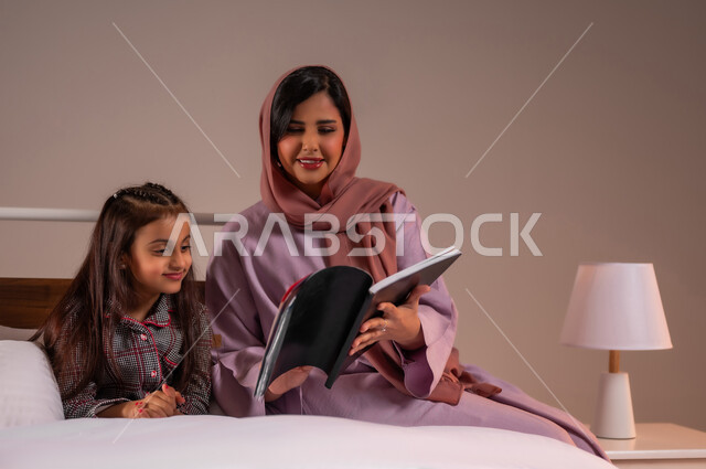 قضاء وقت ممتع مع الابنه، مفهوم التربيه القائمه على الحب والحنان، المشاركه بقراءه القصص المفيده مع الأبناء قبل النوم، بورتريه لامرأة عربية خليجية سعودية تقرأ الروايات المسليه لابنتها، خلفية ملونة