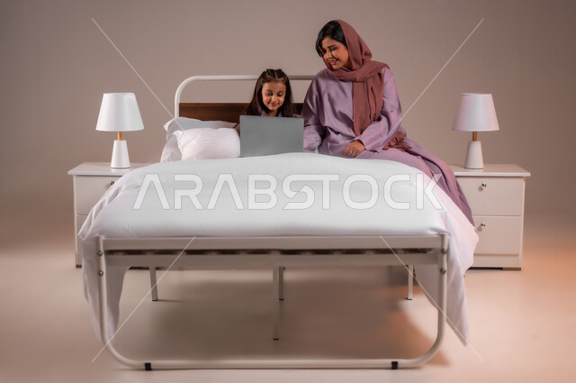 The concept of distance learning using modern technical devices and technology, taking responsibility and caring for children, following lessons online, the Saudi family and its role in raising and creating future generations, a portrait of a veiled Saudi Gulf Arab woman helping her daughter with her lessons, a colorful background