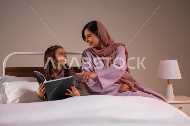 المشاركه بقراءه القصص المفيده مع الأبناء قبل النوم، مفهوم التربيه القائمه على الحب والحنان، بورتريه لامرأة عربية خليجية سعودية تقرأ الروايات المسليه لابنتها، قضاء وقت ممتع مع الأبنه قبل النوم، خلفية ملونة