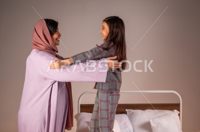 The concept of caring for and paying attention to children, the benefits of early sleep, a portrait of a veiled Saudi Arabian Gulf woman preparing her daughter for sleep, relaxing and enjoying the calm atmosphere, following a healthy lifestyle, a colorful background