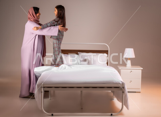 فوائد النوم المبكر للجسم، مفهوم العناية والاهتمام بالأبناء، بورتريه لامرأة عربية خليجية سعودية محجبة تقوم بتحضير ابنتها للنوم، الاسترخاء والاستمتاع بالأجواء الهادئة، اتباع أسلوب حياة صحي، خلفية ملونة