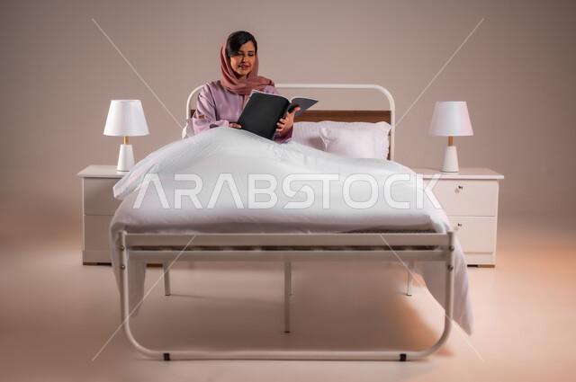 الاسترخاء والاستمتاع بالأجواء الهادئة، قراءة الروايات والقصص الممتعة، الشعور بالراحة والطمأنينة, بورتريه لسيدة عربية خليجية سعودية مبتسمة تجلس في سرير مريح تمسك بيدها الكتاب، اتباع أسلوب حياة صحي، خلفية ملونة