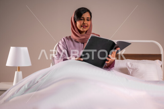 قراءة الروايات والقصص الممتعة، الشعور بالراحة والطمأنينة, بورتريه لسيدة عربية خليجية سعودية مبتسمة تجلس في سرير مريح تمسك بيدها الكتاب، الاسترخاء والاستمتاع بالأجواء الهادئة، اتباع أسلوب حياة صحي، خلفية ملونة