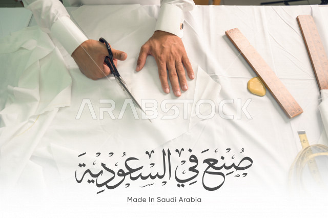 شاب سعودي خليجي يعمل في مهنة الخياطة ، يستخدم الأدوات المناسبة لتفصيل جلابية خاصة لاحدى الزبائن ، محل خياطة و تفصيل الملابس الرجالي في السعودية ، مهارة الخياطة واتقان تفصيل الملابس الشبابية  ، صناعات سعودية ، الانتاج السعودي للملابس ،مخطوطة صنع في السعودي