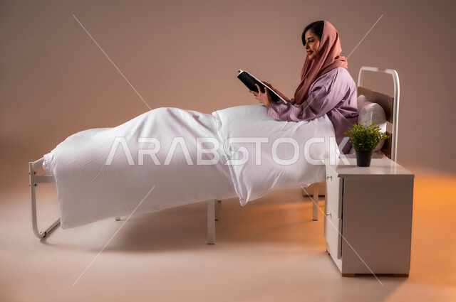 الاسترخاء والاستمتاع بالأجواء الهادئة، الشعور بالراحة والطمأنينة, قراءة الروايات والقصص الممتعة، بورتريه لسيدة عربية خليجية سعودية مبتسمة تجلس في سرير مريح تمسك بيدها الكتاب، اتباع أسلوب حياة صحي، خلفية ملونة