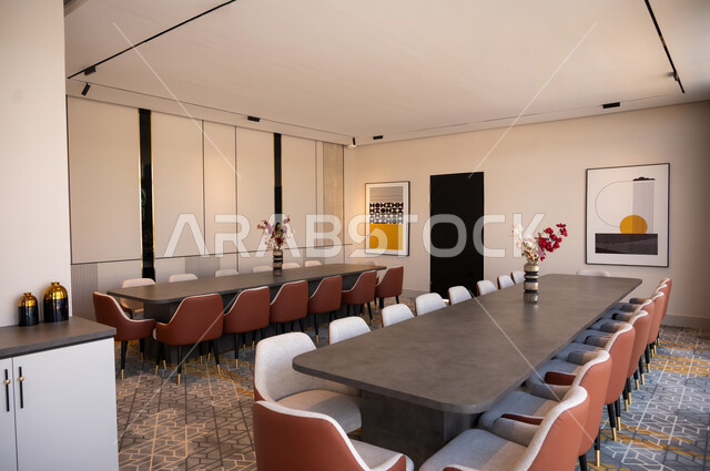 غرف مكتبية بتصاميم وديكورات داخلية فخمة مع أثاث فاخر ومريح، التصميم العصري الحديث للمكاتب في الشركات في السعودية، غرفة اجتماعات واسعة مع طاولات محاطة بكراسي، لوحات فنية معلقة، الفن الهندسي المعماري المتطور