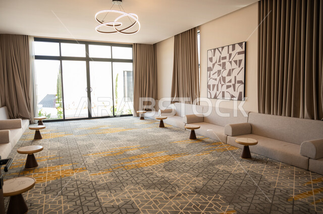 نوافذ وواجهات زجاجية المطلة على الحديقة الخارجية، الديكورات الداخلية الراقية للفلل والشقق السكنية في المملكة العربية السعودية، غرفة معيشة مع أثاث منزلي فاخر باللون البيج، التصاميم الداخلية لغرف الجلوس المريحة على الطراز الحديث