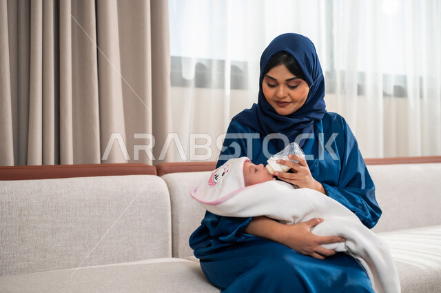 قضاء أوقات ممتعة مع الأطفال، الأسرة وتحمل المسؤولية، دور و حنان الأم في رعايه أبنائها, سيدة عربيه خليجيه سعوديه ترتدي العباءة تحمل ابنتها وتقوم بإعطاءها الحليب الصناعي من عبوه الرضاعه, ايماءات تدل على الحب والحنان, مفهوم الأمومه والرضاعه الصناعيه
